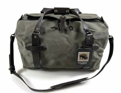 Green duffle bag with leather straps and tag.