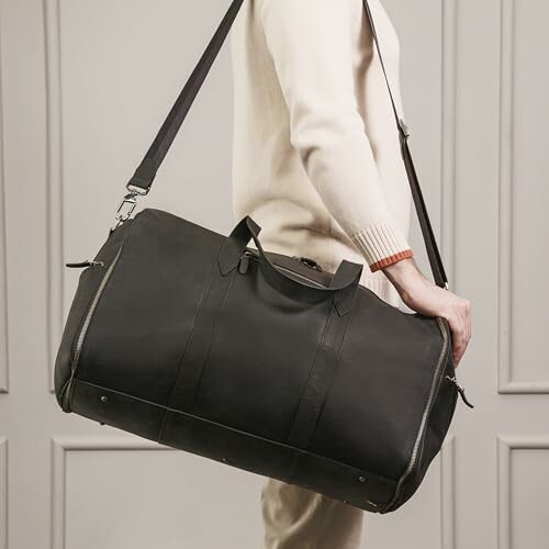 Person carrying a large black duffel bag with shoulder strap.